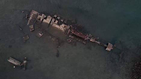 Aerial-birds-eye-view-of-a-sunken-rusty-ship-in-shallow-waters-near-Port-Badjanan-at-Moroni,-Comoros