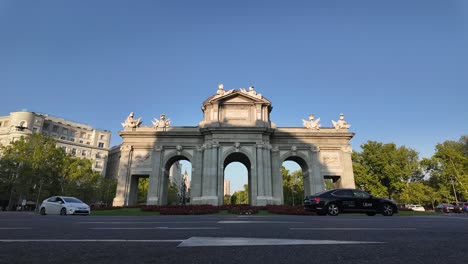 Vista-En-ángulo-Bajo-De-La-Puerta-De-Alcalá-En-La-Ciudad-De-Madrid,-España,-Con-Tráfico-Fluido-En-Una-Tarde-Soleada-Antes-Del-Atardecer