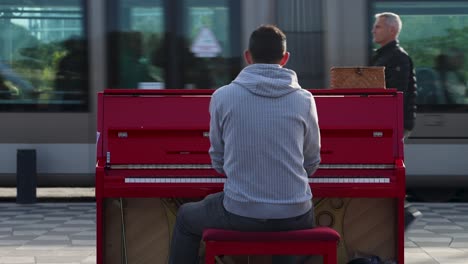 Tram-passes-by-street-performer-playing-piano-in-Nice,-France,-medium-static-shot-from-behind