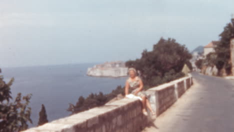 Carretera-Costera-Con-Mujer-Caucásica-Sentada-En-El-Malecón-De-Dubrovnik,-Década-De-1960