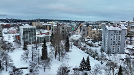 Aerial-view-over-a-snowy-park,-toward-downtown-Lahti,-winter-evening-in-Finland