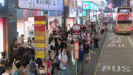 From-a-bus's-high-viewpoint,-a-nighttime-scene-in-Hong-Kong's-Mong-Kok-area-shows-hundreds-of-commuters-waiting-at-bus-stops-on-the-bustling-streets-of-Kowloon