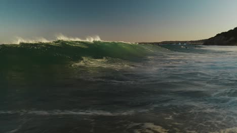 Niedrige-Luftaufnahme,-Die-Vor-Einer-Brechenden-Welle-Fliegt,-Die-Bei-Sonnenuntergang-Hinter-Einem-Bodyboarder-Herläuft