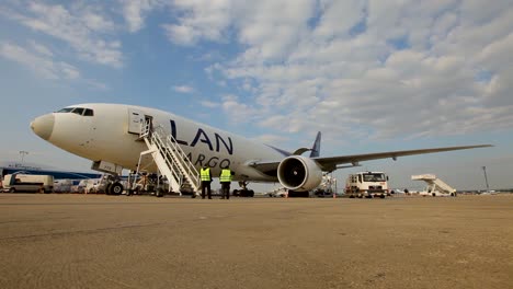 Frachtflugzeug-Wird-Am-Flughafen-Mit-Arbeitern-Und-Bodenfahrzeugen-Unter-Blauem-Himmel-Beladen