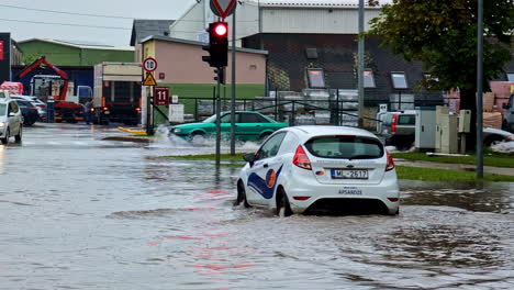 Vehicles-drive-cautiously-through-deep-water-on-a-flooded-city-street-following-intense-rain