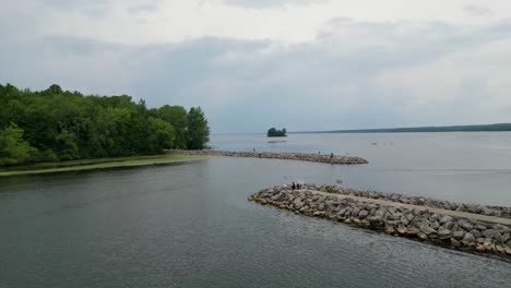 A-serene-aerial-view-of-a-calm-lake-bordered-by-green-trees,-with-rocky-breakwaters-extending-into-the-water