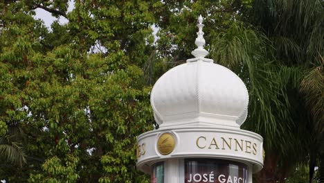 Cannes-Schild-Auf-Drehender-Litfaßsäule-Mit-Grünen-Bäumen-Im-Hintergrund