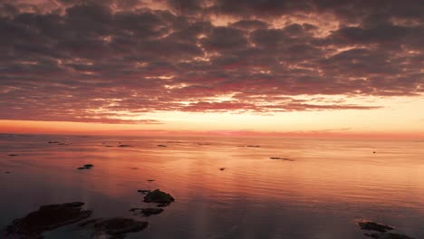 A-serene-aerial-view-of-a-water-landscape-and-heavy-clouds,-highlighted-by-the-dark-orange-light-of-the-setting-sun