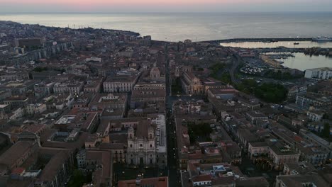 Una-Ciudad-Costera-Al-Anochecer-Con-Edificios-Históricos-Y-Un-Puerto-Animado,-Vista-Aérea