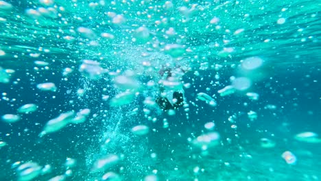 Snorkeler-diving-underwater-surrounded-by-bubbles-in-clear-blue-ocean