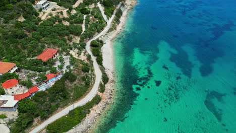 Vista-Aérea-De-Un-Dron-Sobre-Aguas-Turquesas-Del-Mar-Mediterráneo-Y-Casas-Entre-Colinas-Boscosas-En-Grecia