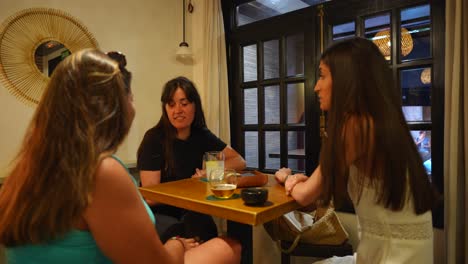 Mujeres-Charlando,-Sonriendo-Y-Disfrutando-De-Bebidas-En-Una-Mesa-De-Pub,-Creando-Un-Ambiente-Cálido-Y-Amigable.