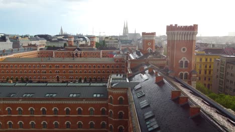 Aerial-dolly-above-black-roofs-and-red-orange-brick-facades-of-buildings-with-towers-in-Vienna-Austria-city-center-as-it-rains