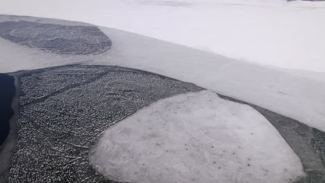 Tilt-up-view-from-above-showcasing-a-frozen-lake-with-mountains-in-the-background-in-Macedonia