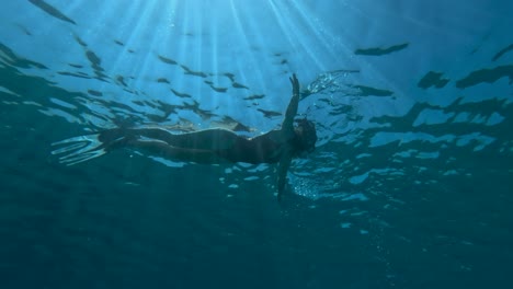 Una-Mujer-Nada-Bajo-El-Agua-En-Una-Piscina-Con-La-Luz-Del-Sol-Filtrándose-A-Través-Del-Agua,-Creando-Una-Escena-Serena.