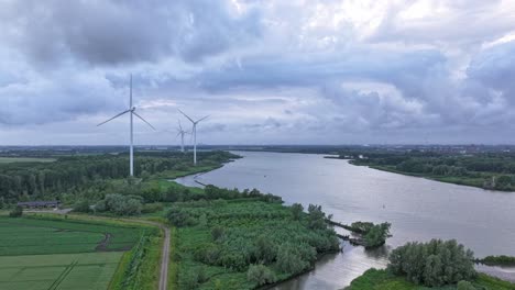 Wind-turbines-near-a-river-on-a-cloudy-day,-aerial-view