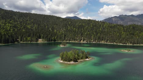 Aerial-footage-of-mountain-lake-Eibsee-beneath-Zugspitze-peak-with-small-islands