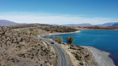 A-bus-drives-around-bend-next-to-Lake-Pukaki,-South-Island-New-Zealand