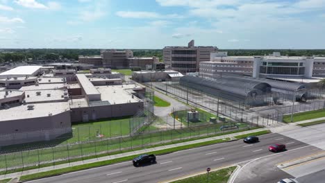 Aerial-view-of-a-high-security-prison-facility,-surrounded-by-barbed-wire-fences-and-adjacent-to-a-main-road