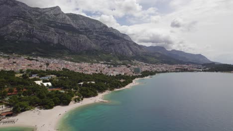 Aerial---Makarska-town-near-Adriatic-sea-and-mountain-range-behind,-Croatia