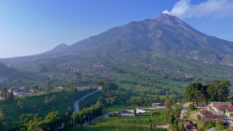 Aerial-view-of-active-volcano-emits-smoke-and-scenery-of-green-tropical-rural-landscape