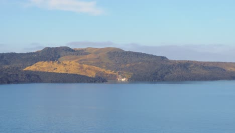 Licht-Leuchtet-Auf-Der-Grünen-Bucht-In-Santorini,-Griechenland-Mit-Friedlichen-Ländlichen-Gebäuden-Entlang-Der-Küste