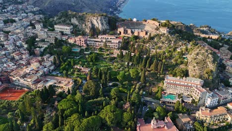 Taormina-with-lush-gardens,-historic-buildings,-and-blue-mediterranean-sea,-aerial-view