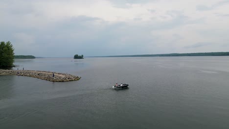 Drone-footage-capturing-a-boat-gliding-across-a-calm-lake-with-a-rocky-shoreline,-perfect-for-aquatic-or-nature-themed-projects