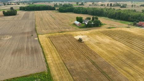 Wide-aerial-view-of-a-harvester-in-a-wheat-field-near-a-farmstead-surrounded-by-trees