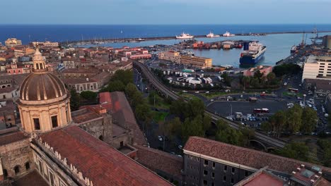 A-coastal-city-port-with-ships-docked-and-buildings-nearby-at-dusk,-aerial-view