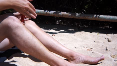 Medium-shot-of-hands-applying-sunscreen-on-legs-at-white-sand-beach-during-daytime