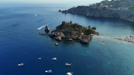 Isola-bella,-sicily,-surrounded-by-boats-on-a-sunny-day,-aerial-view