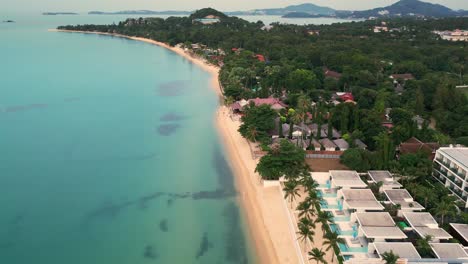 Unique-aerial-view-of-the-Koh-Samui-coast-with-resorts-and-beautiful-clear-water,-copy-space-and-slow-motion