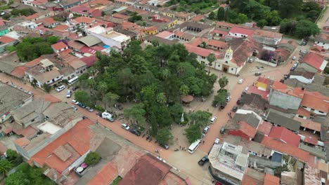 Aerial-orbits-treed-plaza-square,-church-in-small-Latin-American-town