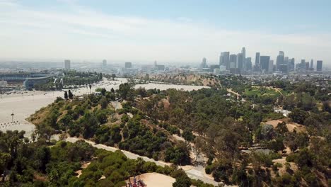 Aerial-backwards-shot-of-Dodger-Stadium,-Park-and-Skyline-of-Los-Angeles-in-background