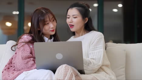 two-attractive-young-girls-surfing-internet-or-shopping-online-on-a-laptop-computer-sitting-on-the-sofa-at-home