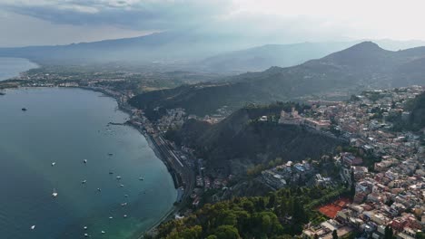 Taormina-coastline-with-lush-hills-and-calm-sea,-boats-dotting-the-water,-aerial-view