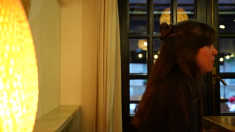 Profile-of-a-caucasian-woman-with-a-bun-chatting-inside-a-restaurant-with-warm-light