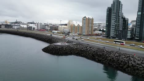 Das-Video-Zeigt-Eine-Luftaufnahme-Von-Reykjavik-Island-Mit-Einer-Felsigen-Ufermauer-Und-Einer-Modernen-Skulptur-Im-Vordergrund