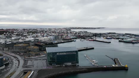 An-aerial-view-of-the-harbor-in-Reykjavik-shows-boats-and-ships-and-buildings-along-the-shore-with-calm-water-and-overcast-sky