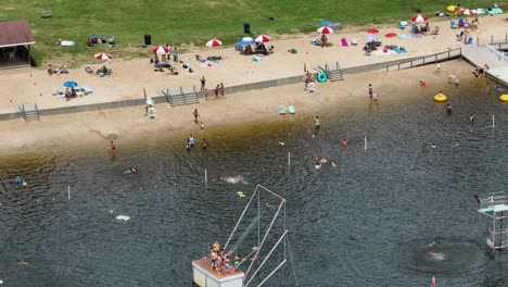 Aerial-top-down-of-many-kids-and-families-having-fun-in-natural-lake-with-beach