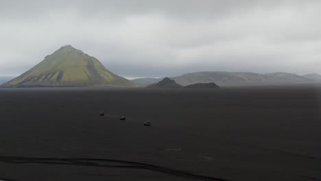 Aerial-orbit-shot-of-cars-on-landscape-of-Iceland-in-front-of-Maelifell-Volcano-during-foggy-day