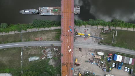 Vista-Aérea-De-Arriba-Hacia-Abajo-Con-Vistas-Al-Sitio-De-Construcción-Del-Puente-Para-Peatones-Y-Bicicletas-Sobre-El-Río-Warta-En-Poznan,-Polonia,-Durante-Un-Día-Soleado-De-Verano