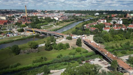 Vista-Aérea-Panorámica-A-La-Izquierda-Con-Vistas-Al-Sitio-De-Construcción-De-Dos-Puentes-Para-Peatones-Y-Bicicletas-Sobre-El-Río-Warta-En-Poznan,-Polonia,-Durante-Un-Día-Soleado-De-Verano.