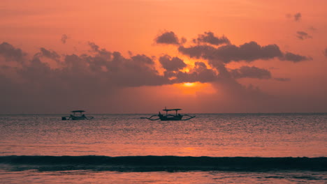 Witness-the-stunning-sunset-at-Jimbaran-Beach-as-traditional-boats-float-on-the-tranquil-waters,-reflecting-the-vibrant-hues-of-the-orange-sunset