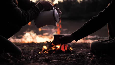 Genießen-Sie-Eine-Ruhige-Lagerfeuerszene-Mit-Dieser-Intimen-Aufnahme-Von-Zwei-Personen,-Die-Wasser-Aus-Einem-Kessel-Gießen