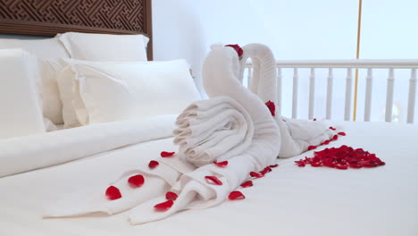 Swan-shaped-towel-art-adorned-with-red-rose-petals-on-a-white-bed-in-a-Bali-hotel,-ideal-for-romantic-themes