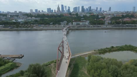 Aerial-view-of-newly-built-pedestrian-and-bicycle-bridge-over-the-Vistula-river-with-Warsaw-skyline-and-skyscrapers-in-view