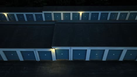 Fotografía-Nocturna-Con-Dron-De-Una-Instalación-De-Almacenamiento-Con-Puertas-De-Garaje-Azules-En-Un-área-Suburbana