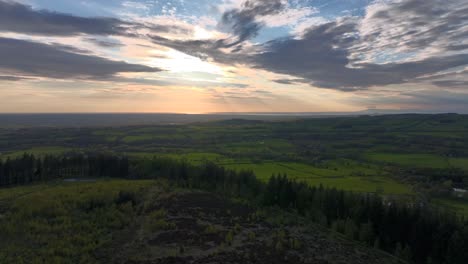 Flying-over-forested-fell-towards-setting-sun-over-English-countryside-at-golden-hour